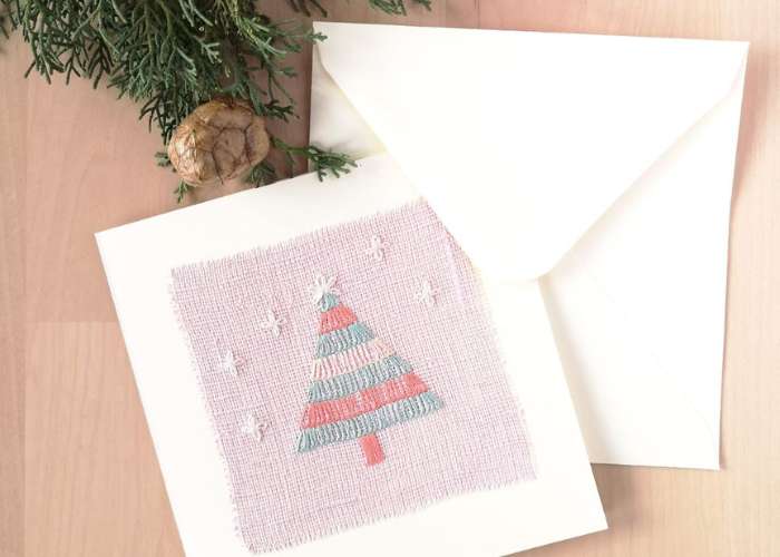 Postkarte mit Weihnachtsbaumstickerei auf rosa Leinen, weißem Umschlag und Tannenzapfen