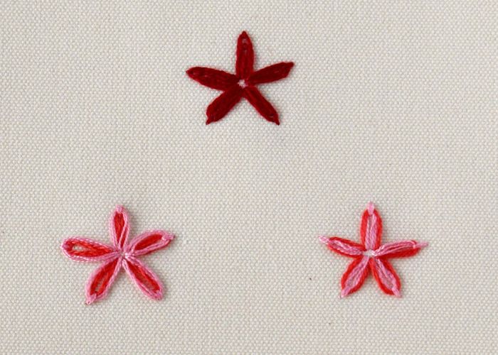 Drei Blumen, gestickt mit Lazy Daisy-Stickerei in roten und rosa Farben