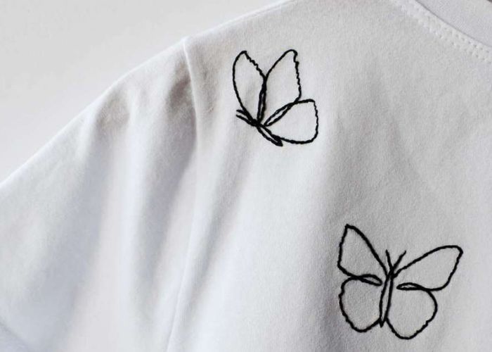 Schwarze Schmetterlingsumrisse auf weißem T-Shirt gestickt